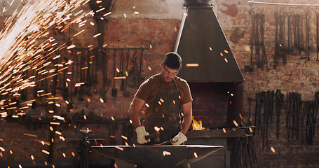 Image showing Hammer, anvil and sparks with a man at work in a forge for metal work manufacturing or production. Industry, welding and trade with a male blacksmith working in a factory, plant or industrial foundry