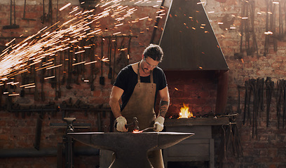 Image showing Hammer, anvil and fire with a man working in a plant for metal work manufacturing or production. Industry, welding and trade with a male blacksmith at work in a factory, forge or industrial workshop