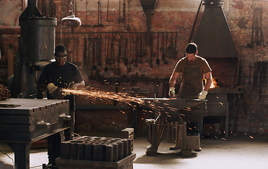 Image showing Hammer, anvil and sparks with men working in a forge for metal work manufacturing or production. Industry, welding and trade with a young male blacksmith in a workshop, plant or industrial foundry