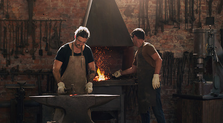 Image showing Hammer, anvil and fire with men working in a foundry for metal work manufacturing or production. Industry, welding and trade with blacksmith craftsmen in a steel workshop, plant or industrial forge