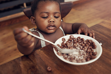 Image showing Black child, cereal and eating baby in a home kitchen with food and bowl at breakfast. African girl, nutrition and youth in a house with hungry kid relax with chocolate fiber snack in the morning