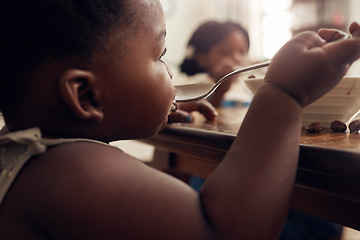 Image showing Black child, cereal spoon and eating baby in a home kitchen with food and bowl at breakfast. African girl, nutrition and youth in a house with hungry kid relax with healthy snack and kids at morning