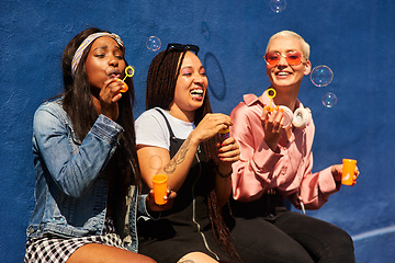 Image showing Happy, friends and women blowing bubbles on vacation, holiday travel or bonding activity and against a blue wall. Happy, game and ladies playing with soap or wand toy or in freedom and social break