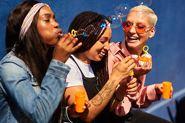 Image showing Women, friends, and blowing bubbles on summer vacation, holiday travel or bonding activity and against a blue wall. Happy, game and ladies playing with soap or wand toy or in freedom and social break