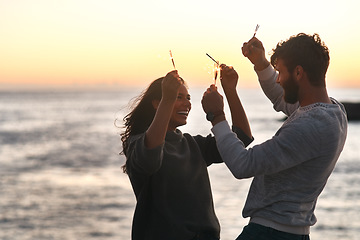 Image showing Sunset, beach and couple with sparklers for celebration, party and quality time on romantic date. Nature, love and happy man and woman with fireworks for honeymoon on holiday, weekend and vacation