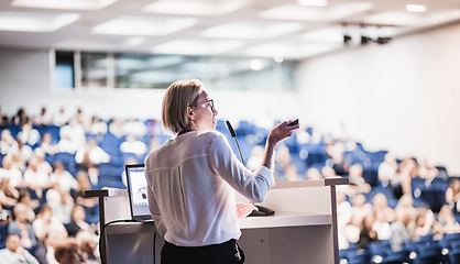 Image showing Female speaker giving a talk on corporate business conference. Unrecognizable people in audience at conference hall. Business and Entrepreneurship event.