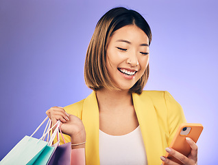 Image showing Asian woman, phone and shopping bag in studio, texting and smile for deal, sale or discount by background. Japanese girl, retail and happy with social media, contact and luxury by purple background