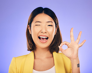 Image showing Portrait, smile and Asian woman with ok sign, wink and emoji against a studio background. Face, female person and model with happiness, hand gesture and symbol for thank you, perfect and approval