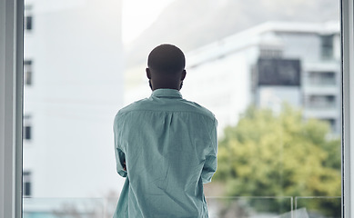 Image showing Back, thinking and window with a business black man standing in his office looking at a city view. Idea, motivation and inspiration with a male employee at work, contemplating a decision in town