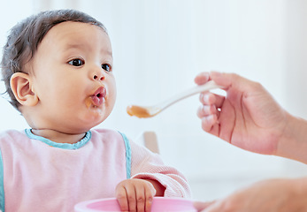 Image showing Mother, feeding baby girl and spoon in home, kitchen or living room for nutrition, growth or health. Woman, hand and food for infant child for help, eating or balance in diet for development in house