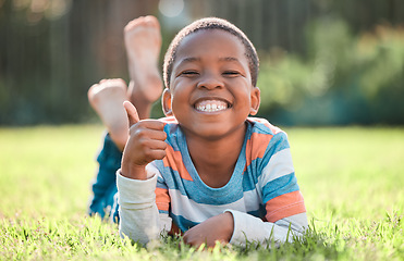 Image showing Thumbs up, portrait of black boy and lying on grass in a nature park with a lens flare. Good news or thank you, success or winner and happy or excited young male child relaxing on a lawn outdoors