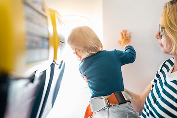 Image showing Mom and child flying by plane. Mother holding and playing with her infant baby boy child in her lap during economy comercial flight. Concept photo of air travel with baby. Real people.