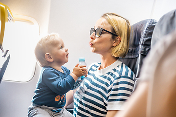 Image showing Mom and child flying by plane. Mother holding and playing with her infant baby boy child in her lap during economy comercial flight. Concept photo of air travel with baby. Real people.