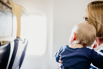 Image showing Mom and child flying by plane. Mother holding and playing with her infant baby boy child in her lap during economy comercial flight. Concept photo of air travel with baby. Real people.