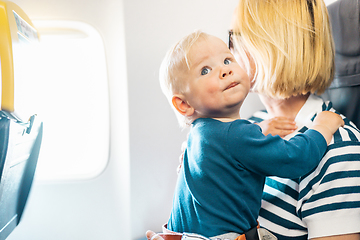 Image showing Mom and child flying by plane. Mother holding and playing with her infant baby boy child in her lap during economy comercial flight. Concept photo of air travel with baby. Real people.