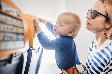 Image showing Mom and child flying by plane. Mother holding and playing with her infant baby boy child in her lap during economy comercial flight. Concept photo of air travel with baby. Real people.