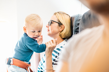 Image showing Mom and child flying by plane. Mother holding and playing with her infant baby boy child in her lap during economy comercial flight. Concept photo of air travel with baby. Real people.