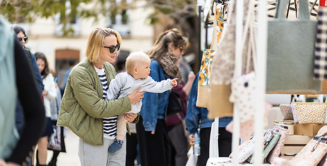 Image showing Mother walking carrying his infant baby boy child in crowd of people wisiting sunday flea market in Malaga, Spain