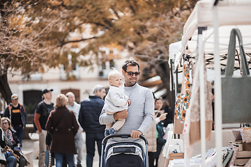 Image showing Father walking carrying his infant baby boy child and pushing stroller in crowd of people wisiting sunday flea market in Malaga, Spain