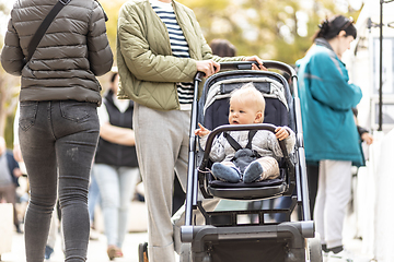 Image showing Mother walking and pushing his infant baby boy child in stroller in crowd of people wisiting sunday flea market in Malaga, Spain.