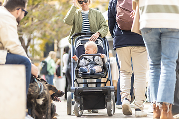 Image showing Mother walking and pushing his infant baby boy child in stroller in crowd of people wisiting sunday flea market in Malaga, Spain.