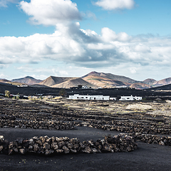 Image showing Traditional white houses in black volcanic landscape of La Geria wine growing region with view of Timanfaya National Park in Lanzarote. Touristic attraction in Lanzarote island, Canary Islands, Spain.