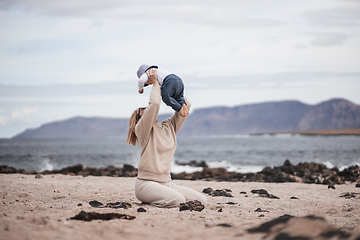 Image showing Mother enjoying winter vacations holding, playing and lifting his infant baby boy son high in the air on sandy beach on Lanzarote island, Spain. Family travel and vacations concept