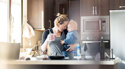 Image showing Happy mother and little infant baby boy together making pancakes for breakfast in domestic kitchen. Family, lifestyle, domestic life, food, healthy eating and people concept.