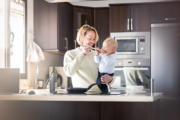 Image showing Happy mother and little infant baby boy cooking and tasting healthy dinner in domestic kitchen. Family, lifestyle, domestic life, food, healthy eating and people concept.