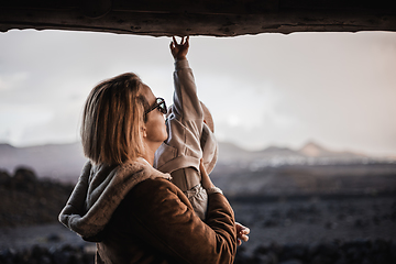 Image showing Mother enjoying winter vacations playing with his infant baby boy son on black sandy volcanic beach of Janubio on Lanzarote island, Spain on windy overcast day. Family travel vacations concept.