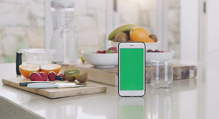 Image showing Phone, green screen and kitchen with fruit, diet app and table by blurred background in home for smoothie. Smartphone, counter and fruits with space for mock up, logo and nutrition brand in house