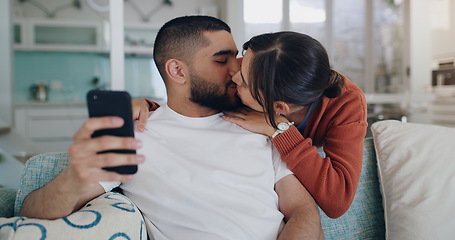 Image showing Love, kiss and couple on sofa with phone, embrace and surfing social media post or or streaming online. Cellphone, man and woman on couch, kissing and hugging in romantic relationship in living room.