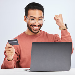 Image showing Laptop, credit card and man excited for online shopping, e commerce and payment in studio. Asian male person with technology and hand to celebrate savings win, promotion or sale on a fintech website