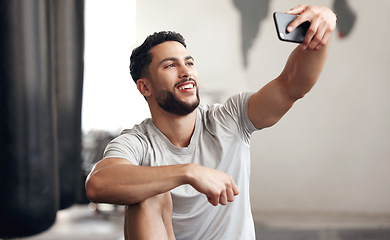 Image showing One fit young hispanic man using a cellphone to take selfies while on a break from exercise in a gym. Happy mixed race guy making video call and taking photos for social media during a rest from trai