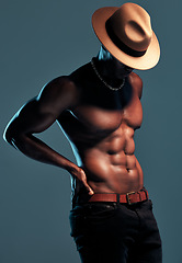 Image showing Black man, topless and sexy fashion model with abs, cow boy style with hat isolated on blue background. Dark, shadow and body with muscular male person, pose with six pack and stylish in studio