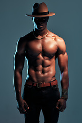 Image showing Black man, shirtless with strong fashion model and sexy, cow boy style with hat isolated on blue background. Dark, shadow and body with muscular male person, pose with six pack and stylish in studio