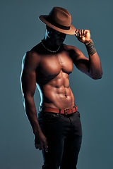 Image showing Black man, shirtless and sexy fashion model with abs, cow boy style with hat isolated on blue background. Dark, shadow and body with muscular male person, pose with six pack and stylish in studio