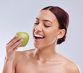 Image showing Apple, happy or woman in studio eating on white background for healthy nutrition or clean diet. Bite, smile or hungry beautiful girl advertising or marketing natural organic green fruits for wellness