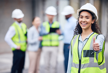 Image showing Thumbs up, woman construction worker and at a industrial workplace happy with her colleagues in the background. Thank you or success, agreement and cheerful or excited architect at building site