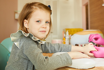 Image showing Little girl in nail salon receiving manicure by beautician. Little girl getting manicure at beauty salon.