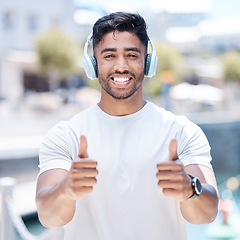 Image showing Happy man, headphones and listening to music with thumbs up for winning, fitness or success in city. Portrait of male person, athlete or runner with headset, thumb emoji or yes sign for audio track