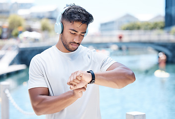 Image showing Fitness, music and man in city with smart watch for running, exercise and tracking workout. Headphones, sports and male person check wristband for marathon training, wellness and performance time