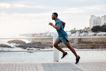 Image showing Black man, runner and exercise outdoor on beach promenade for fitness, training or cardio workout. African athlete, person and running at sea for performance, health and wellness in nature with focus