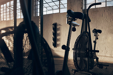 Image showing Spinning bike, empty and gym for exercise with a shadow background at a warehouse with light. Club, cardio bicycle for fitness equipment for training and workout in storage venue in the dark.