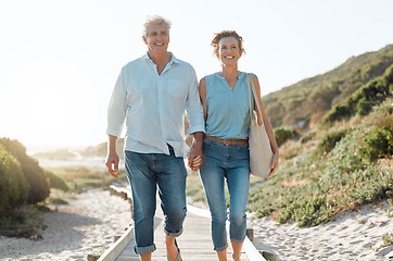 Image showing Senior, couple and walking at the beach with hands in portrait for happiness on a vacation in the outdoor. Mature, woman and man holding by ocean for travel on holiday with sunshine for the weekend.