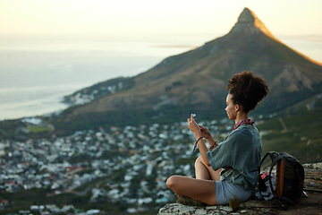 Image showing Woman, hiking and phone on mountain for travel in cape town for wellness on the weekend. Female hiker, mobile and adventure on a cliff with cityscape for scenery of lions head in the outdoor.
