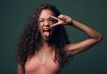 Image showing Tongue out, wink and peace by gen z girl in studio with hand, sign and gesture on green background. Face, fingers and female model with crazy, personality and youth aesthetic, emoji or isolated pose