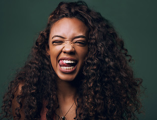 Image showing Tongue out, portrait and young woman in studio with natural curly hair, happy meme or wink on a green background. Face, crazy and female model with funny personality, goofy and silly emoji expression