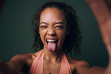 Image showing Selfie, tongue out and young woman in studio with facial, expression or personality on green background. Face, emoji and crazy gen z model wink for silly profile picture, portrait or fun goofy post