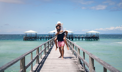 Image showing Couple, piggyback and outdoor beach deck on a tropical island with love and water on holiday. Summer vacation, travel smile and Maldives playful in nature with freedom and happiness by ocean and sea